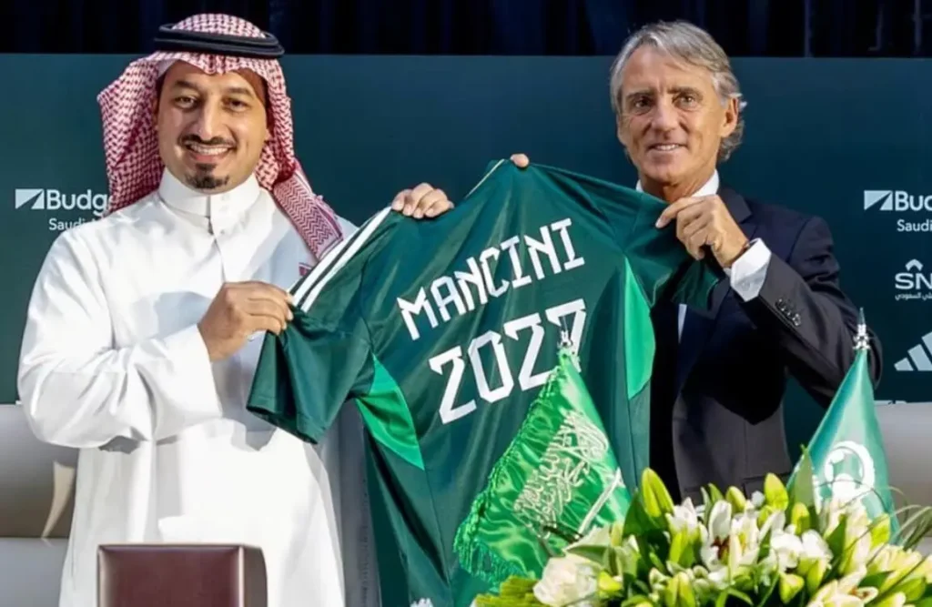 Roberto Mancini holding Saudi Arabian national team jersey.